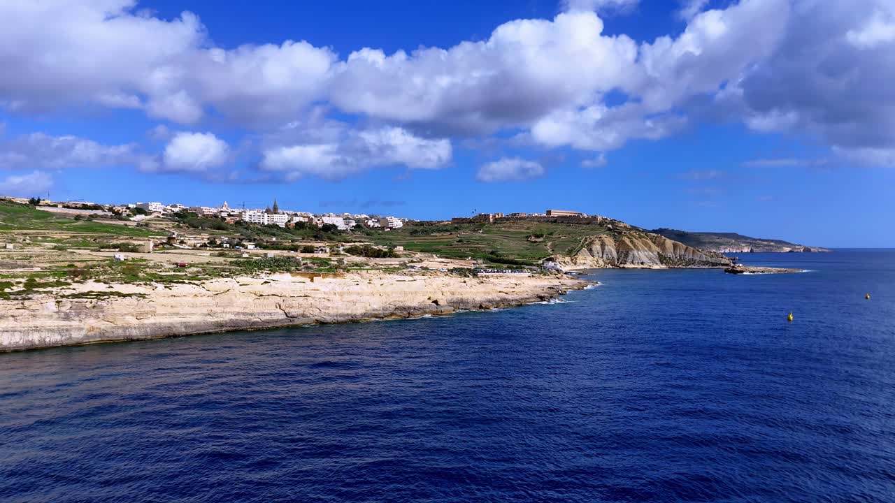 Un panorama mozzafiato dall'alto della costa di Gozo a Malta baciata dal sole in primavera, con vivaci acque blu del Mediterraneo sotto un cielo luminoso con soffici nuvole bianche e scogliere dorate