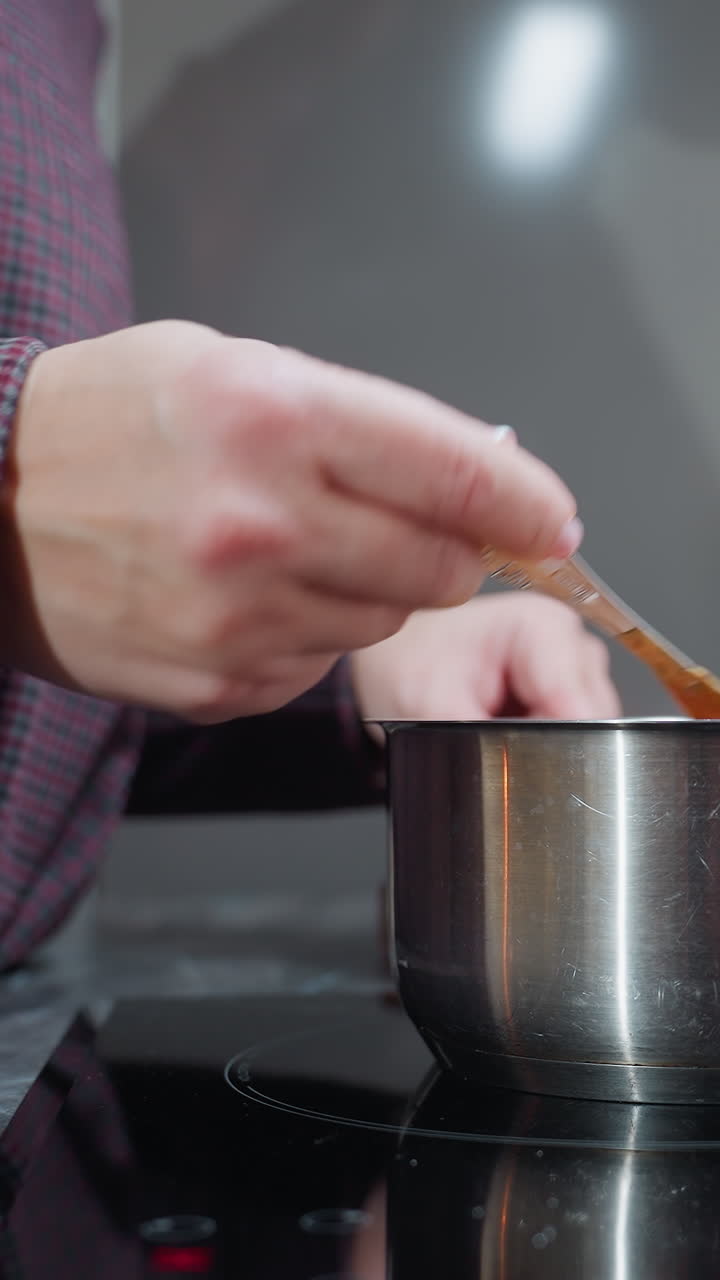 Partial view of woman cooking, stirring steaming soup while holding pot handle, soft lighting casts her shadow on wall, reflecting cozy home kitchen atmosphere