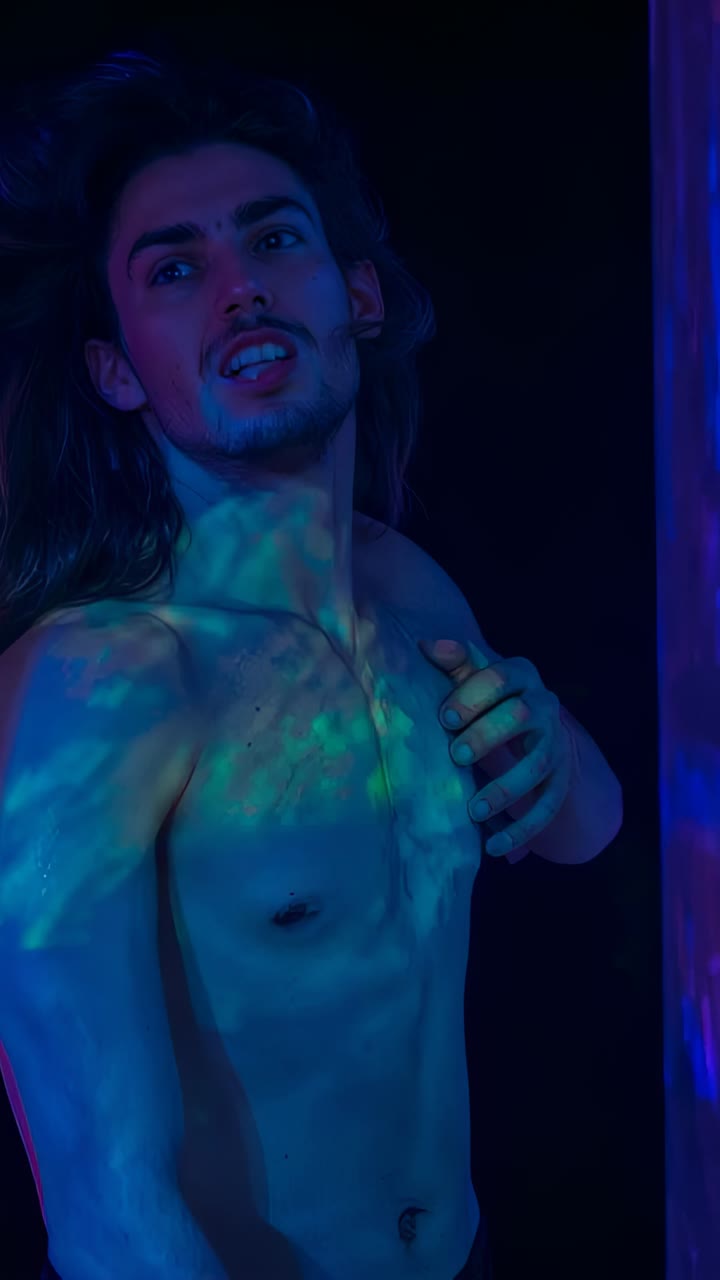 Video verticale: modello maschile a torso nudo che alza lo sguardo, si inclina per lo scatto, con ventilatore e luci in movimento