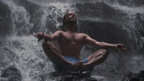 young man meditating under waterfall.