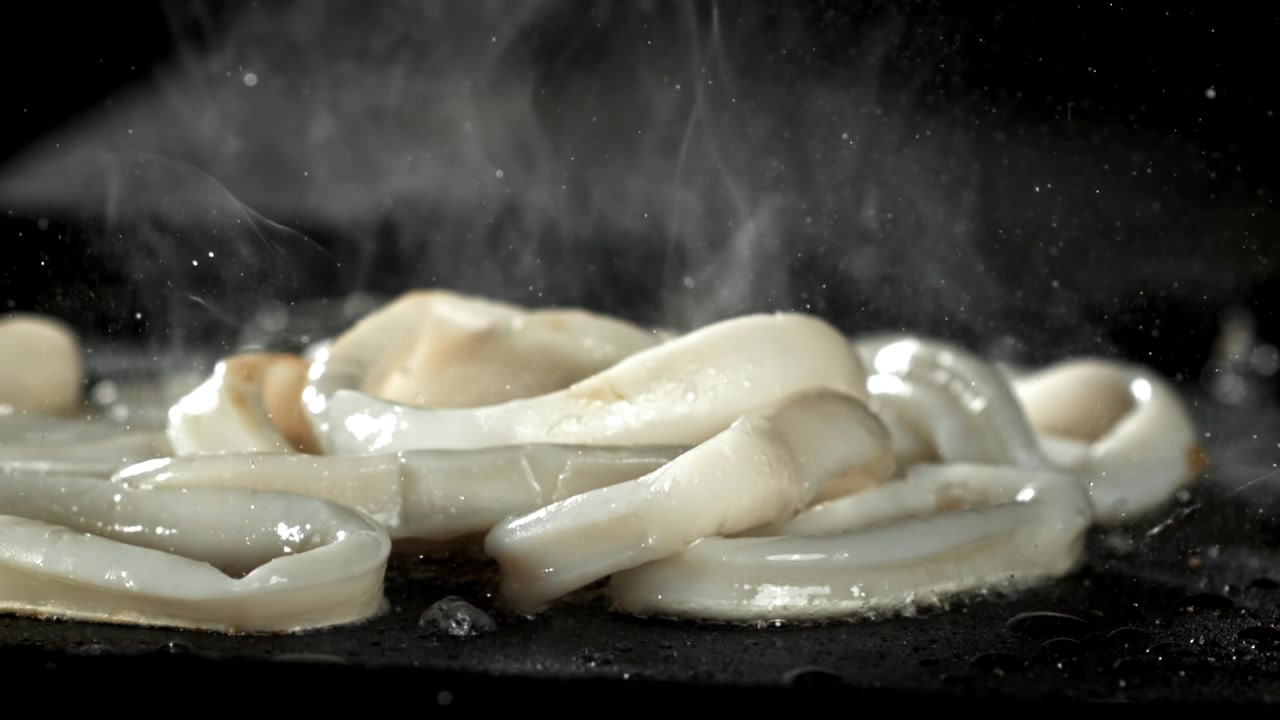 Anelli di calamari freschi che sfrigolano e fumano su una padella calda