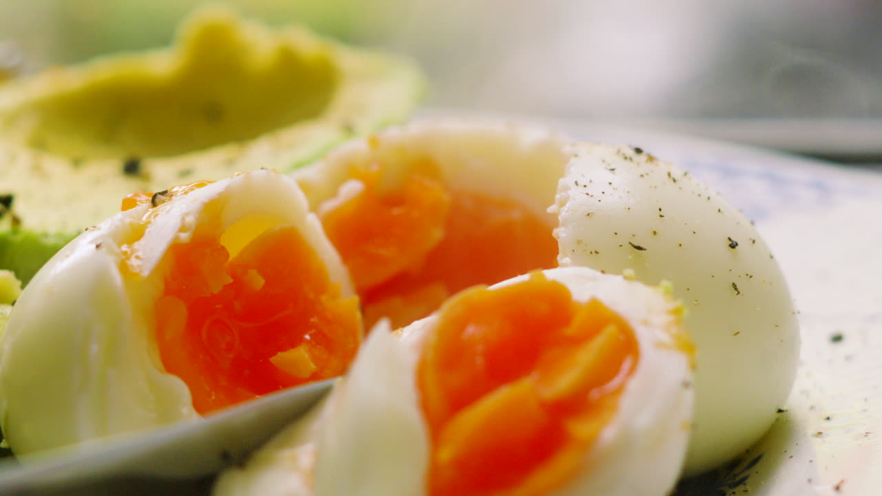 Delicious Freshly Cooked Soft Boiled Eggs on Plate with Ripe Green Avocado Ready to Eat for Healthy Breakfast. High Protein Meal Seasoned with Pepper. Slow Motion Food Clip