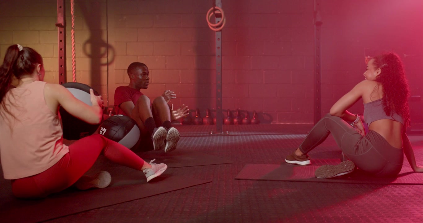 Coach leading two women cueing, showing med ball core work, left walking right holding in gym