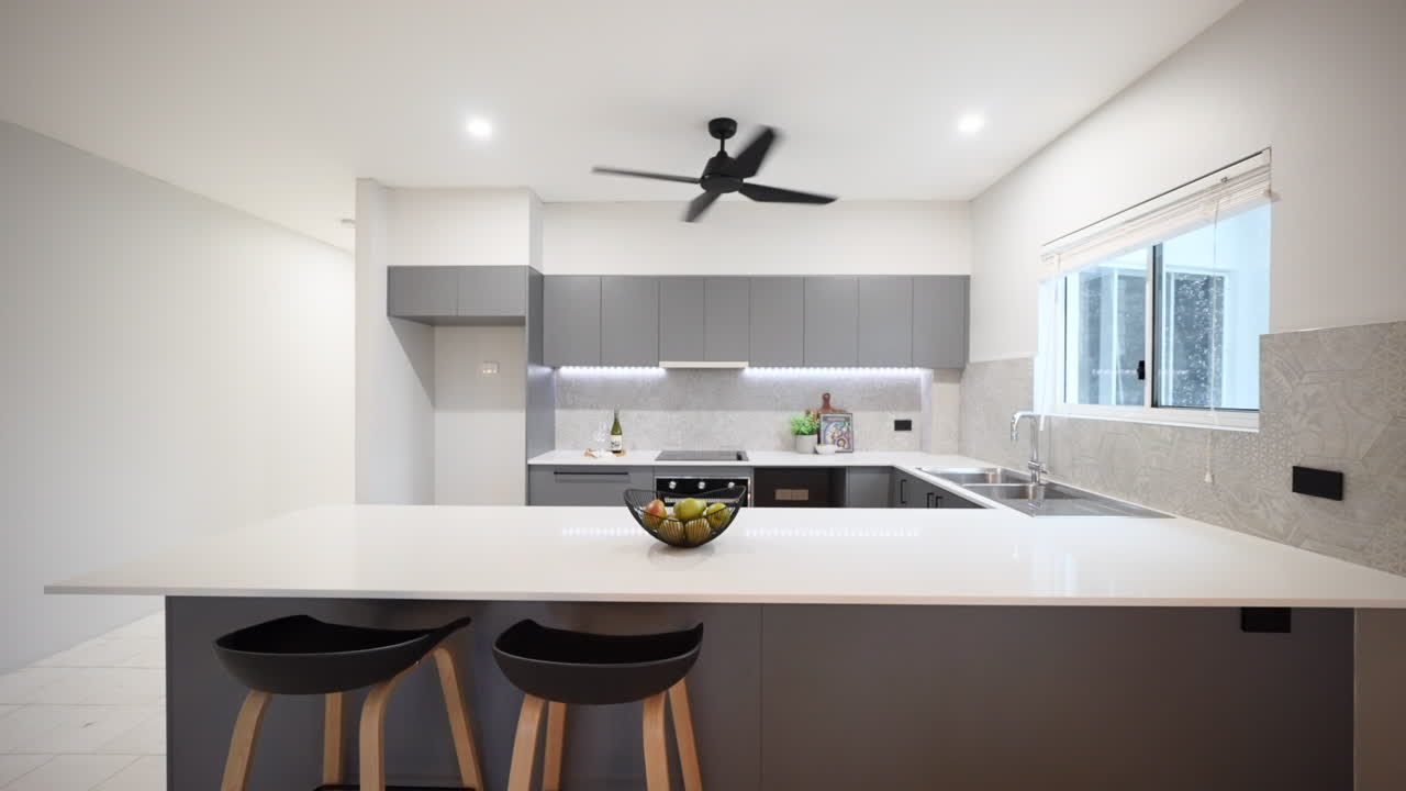 Cocina interior de apartamento moderno y lujoso de color gris, decorada con taburetes negros redondeados en la barra, con peras en un cuenco negro y sin refrigerador.