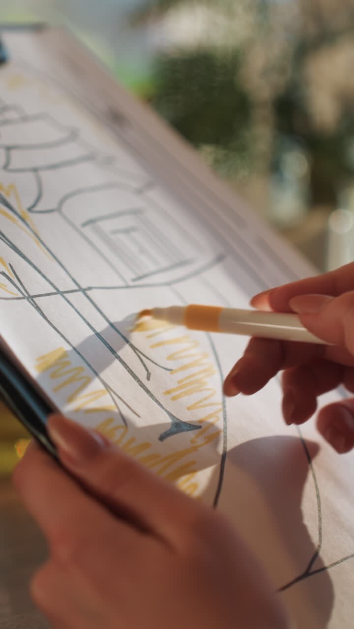 Closeup hands highlighting architectural sketch on clipboard warm sunlight studio focus. Yellow highlighter fills facade shapes while steady fingers hold clipboard paper texture and ink lines show