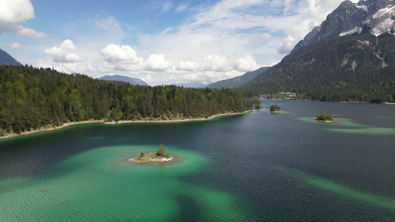 vista aérea del colorido lago eibsee en baviera, alemania, rodeado de pinos y una lejana cordillera montañosa, destacando la tranquila armonía de la naturaleza