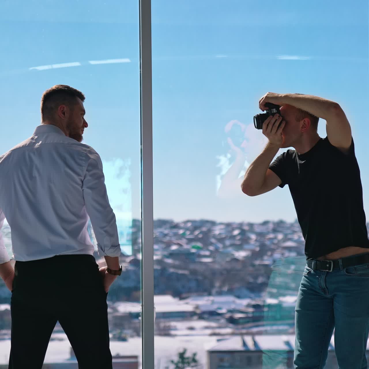 Young man working with camera in office. Businessman posing on camera. Professional photographer taking photos of a male model. Photo session near window