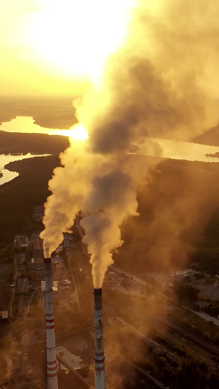 Industrial zone with pipes among nature. Thick white smoke is poured from the factory pipe at sunset. Pollution of the environment. Ecological problems. Aerial view Vertical video