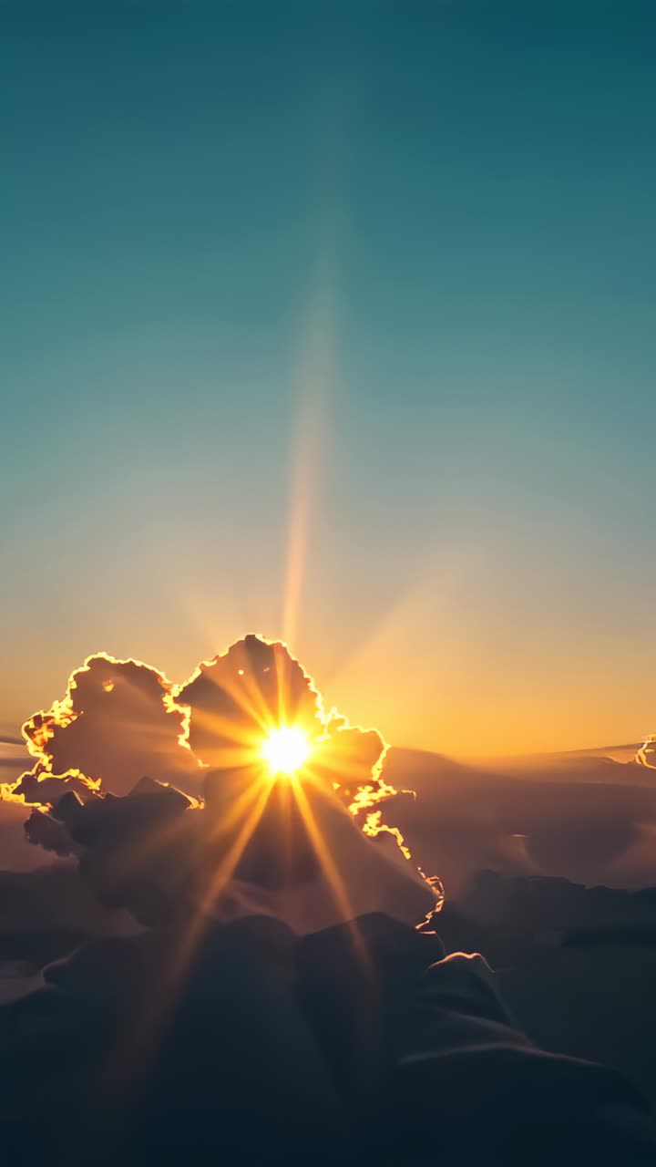 Vertical video: Sun breaking through central cloud sending golden beams across warm sky at dawn
