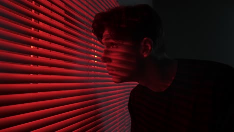 man looking through red blinds
