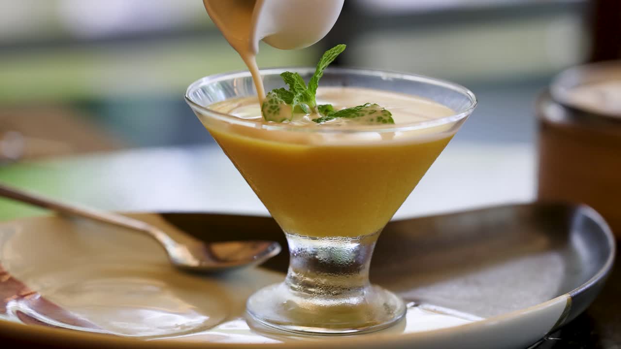 A creamy sauce is elegantly poured over a Thai dessert in a glass, creating a rich, inviting presentation