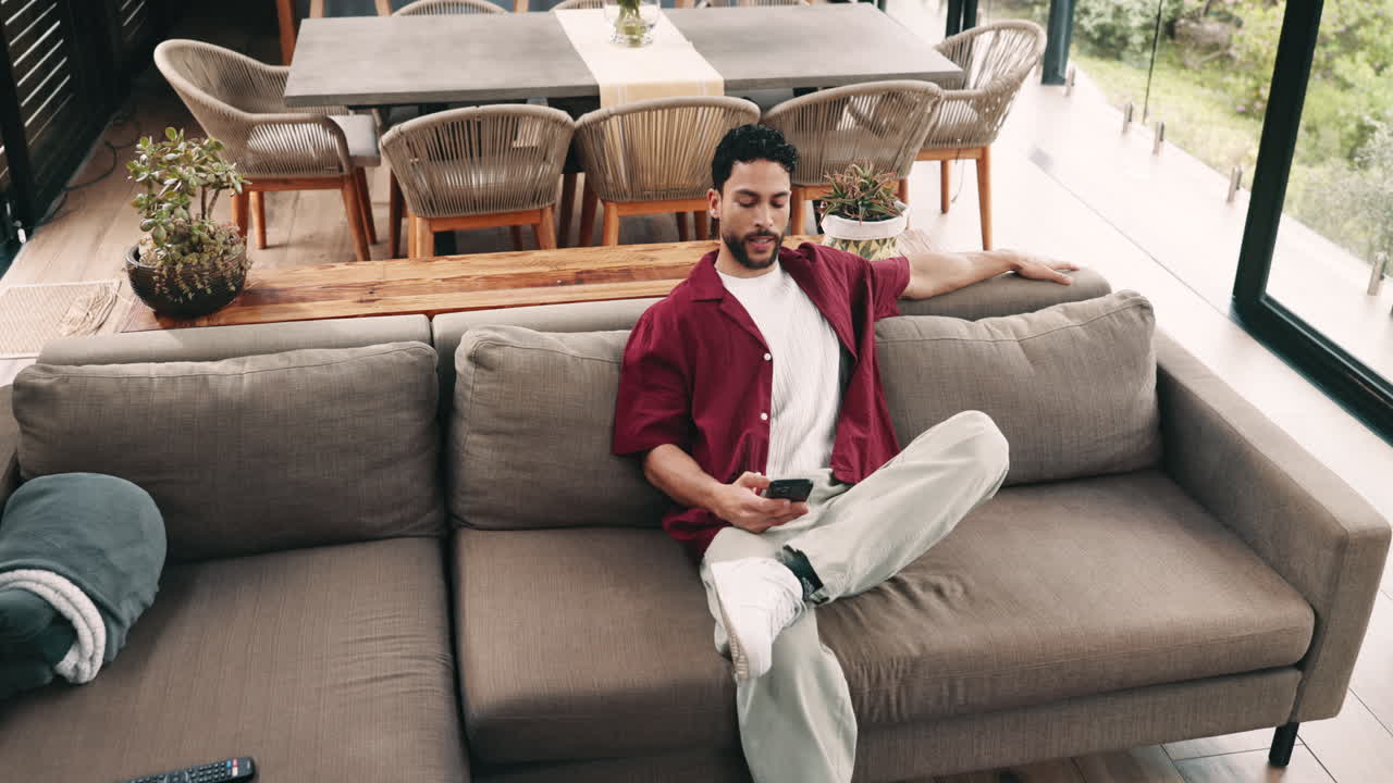 Giovane uomo si rilassa sul divano e usa lo smartphone a casa