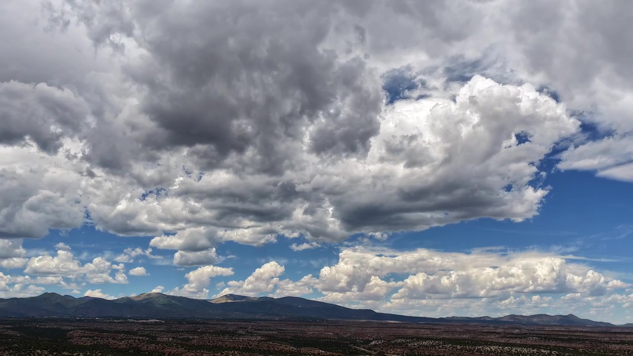 Timelapse 4K con drone di un clima mutevole e formazioni nuvolose dense. Un vasto sistema meteorologico si muove rapidamente nel cielo, proiettando ombre profonde sulle vaste mesas e le aspre montagne del Nuovo Messico