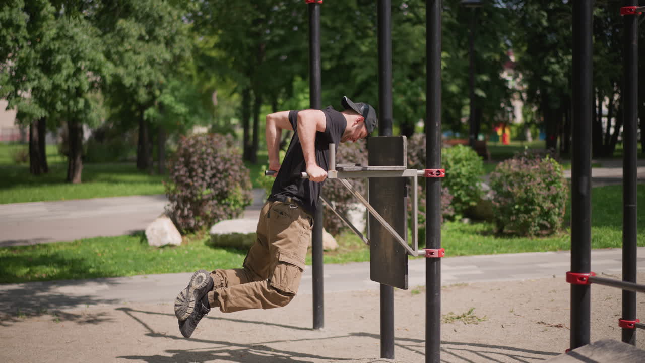 Outdoor Park Parallel Bars Dip Workout, White Male In Cap And Cargo Pants Performing Strict Dips With Focused Grip And Controlled Motion, Sunny Day, Leafy Background, Muscle Tension And Endurance