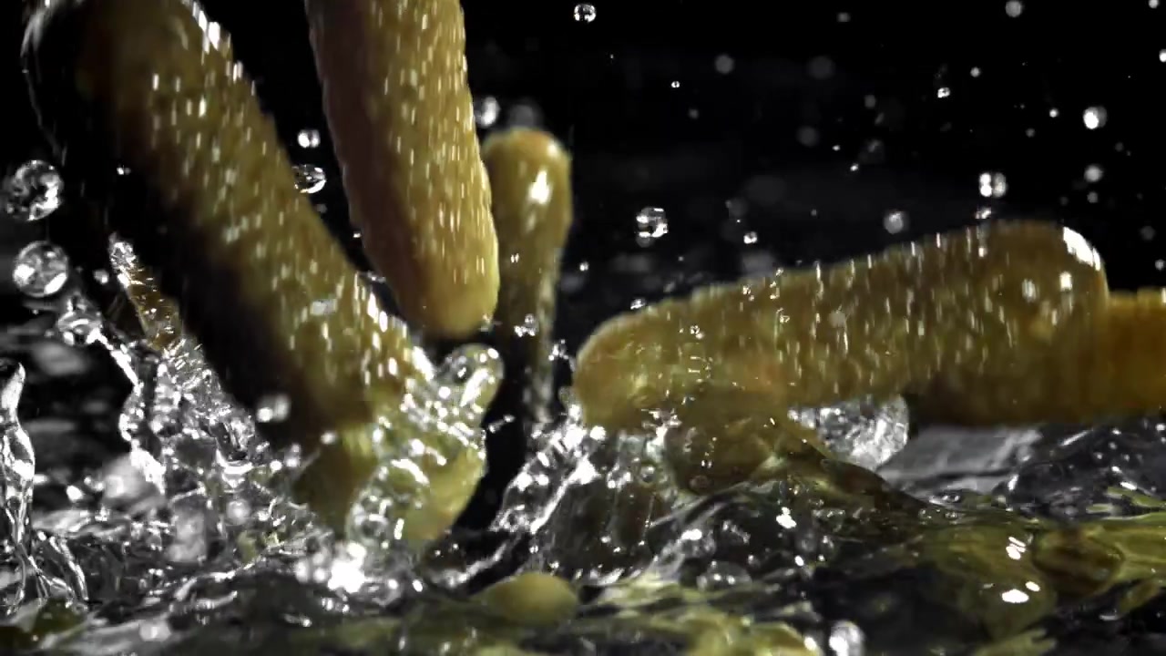 Cetriolini verdi che cadono e schizzano nell'acqua al rallentatore
