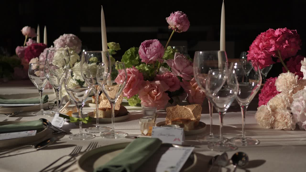Close up of elegant table setting with pink flowers, glassware and candles prepared for event