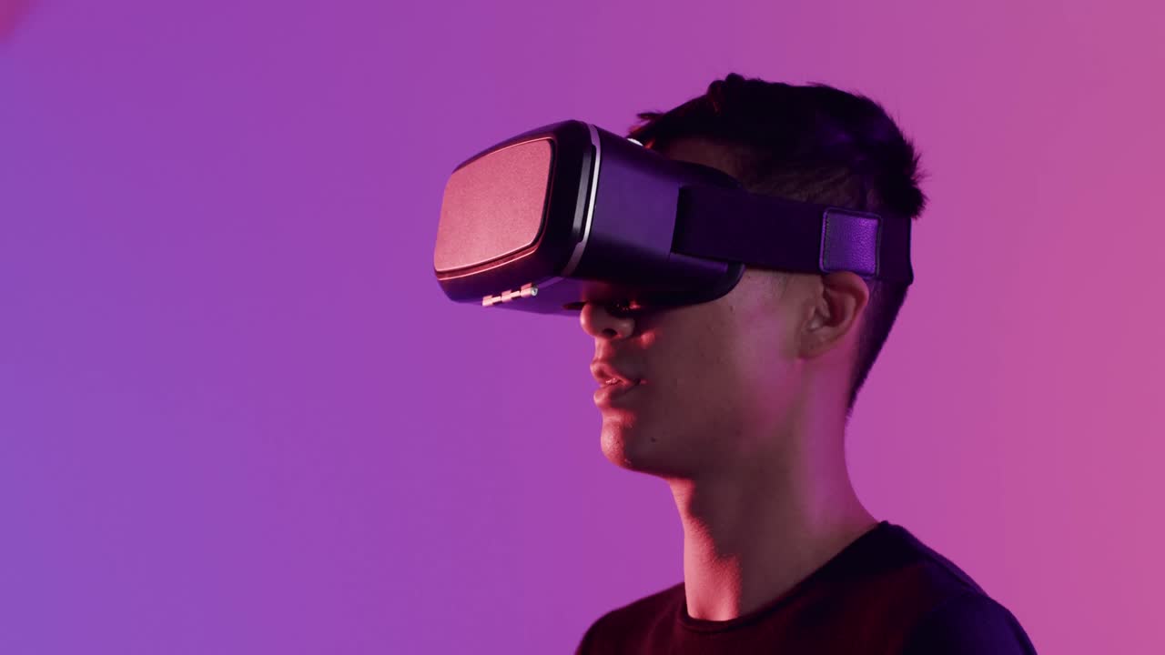 Happy asian man using vr headset on purple background, copy space, slow motion