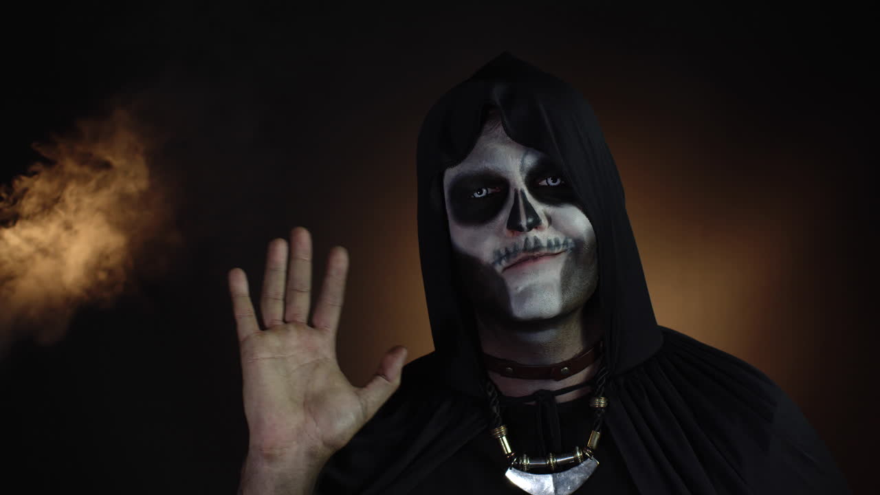hombre aterrador en esqueleto disfraz de halloween agitando las manos mirando a la cámara. hola, hola, saludo