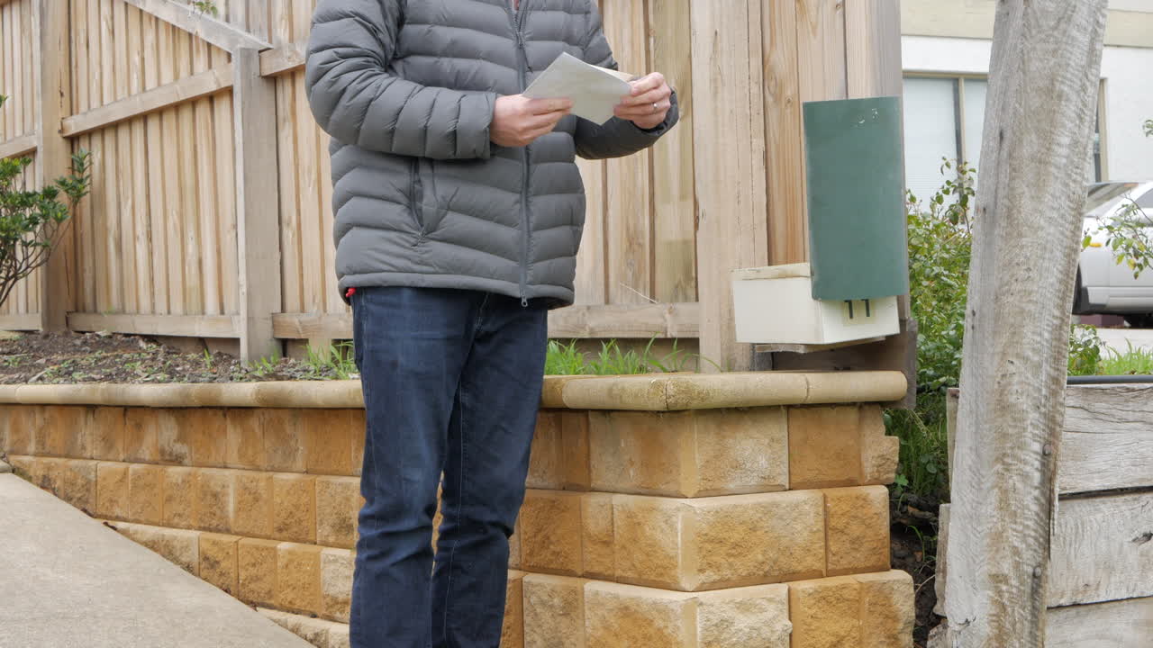 남자는 교외 집의 우편함에서 우편물을 수집합니다