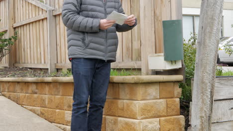 Man-collects-mail-from-the-letter-box-at-a-suburban-house