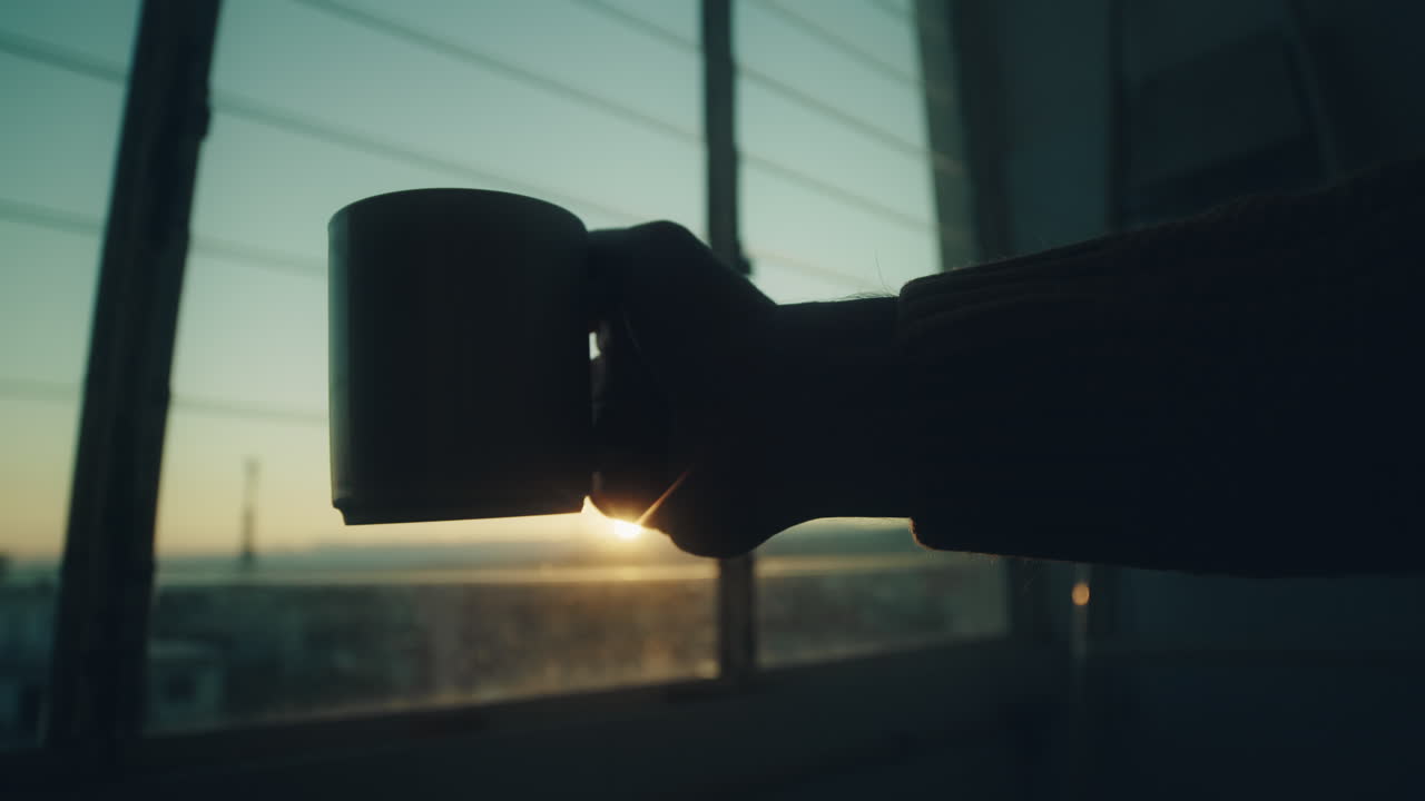 창문 앞에 컵을 들고 있는 손