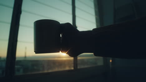 hand holding a cup in front of a window