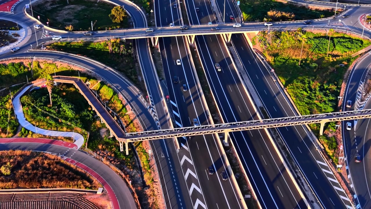 Overhead view of highway interchange with spiral ramp and bridge, Spain. Multilane motorway, curved on-ramp, overpass structure and green vegetation in warm evening light.