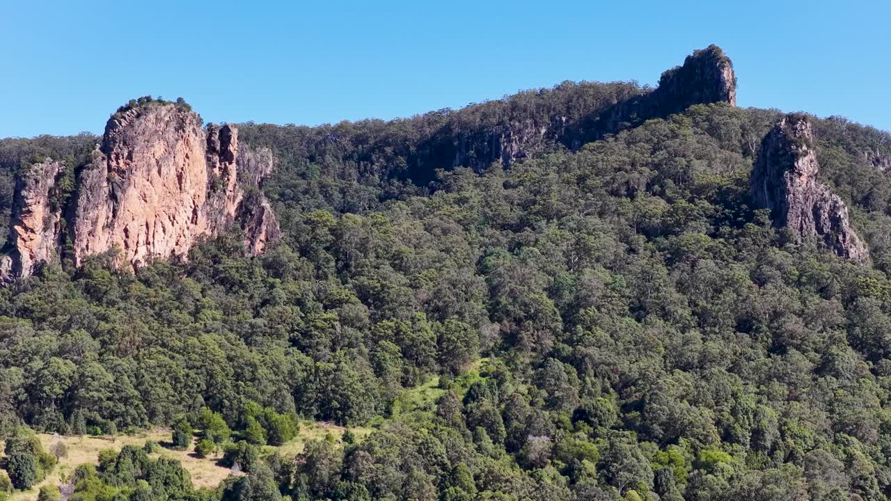 Drone footage captures lush green hills and rocky outcrops under clear blue skies in Nimbin, Australia
