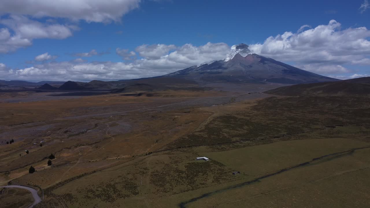 capturar la grandeza del volcán cotopaxi en imágenes de drones de 4k, mientras nuestra cámara se desplaza suavemente a través del majestuoso pico en un día soleado, enmarcado por el cielo azul y adornado con suaves velos de nubes