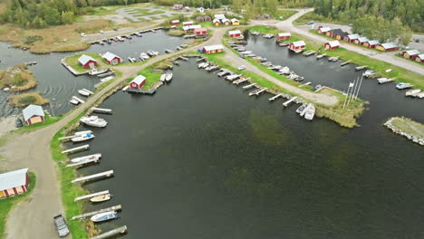 Mooring-Boats-Over-Marina-Near-Typical-Village-With-Red-Houses-In-Finland