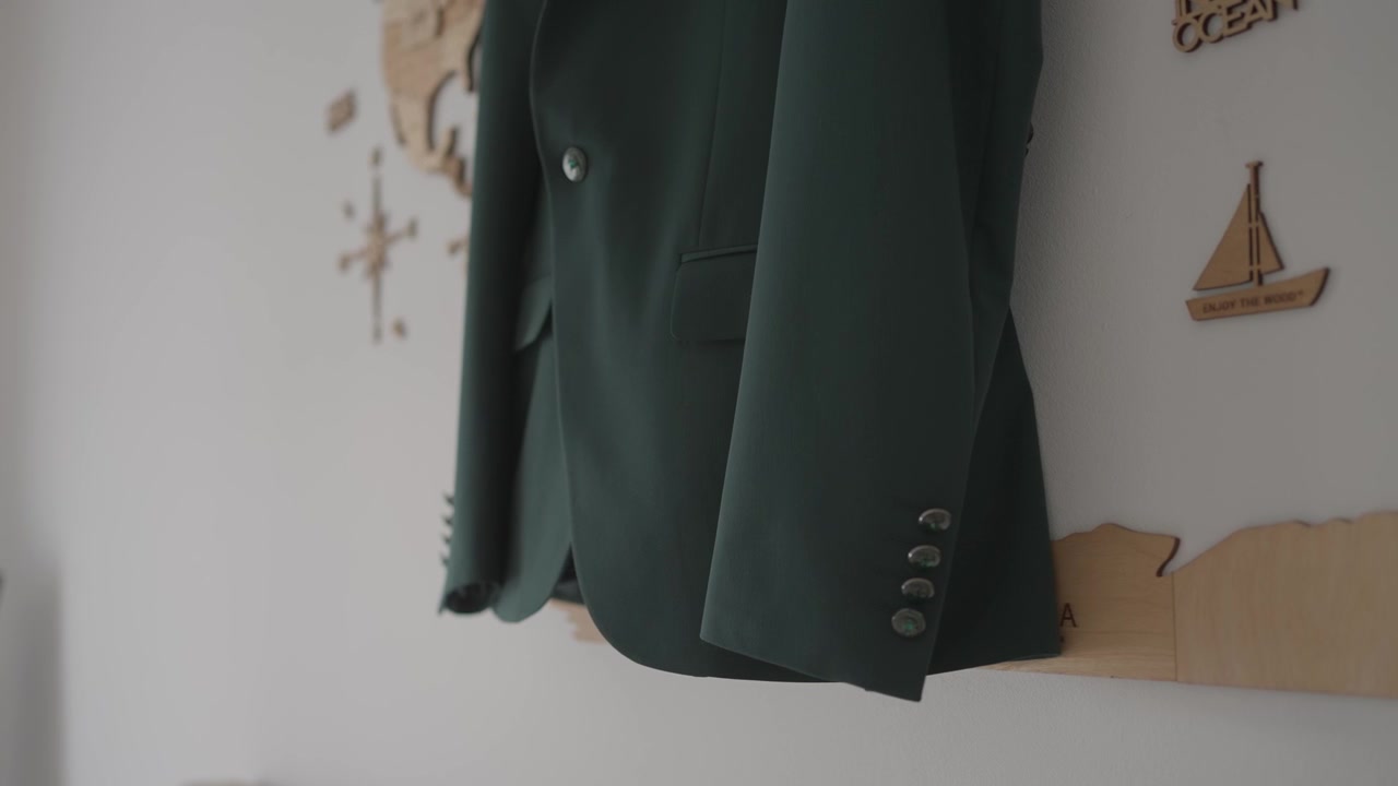 Giacca da abito da sposo verde scuro appesa al muro con sfondo decorativo.