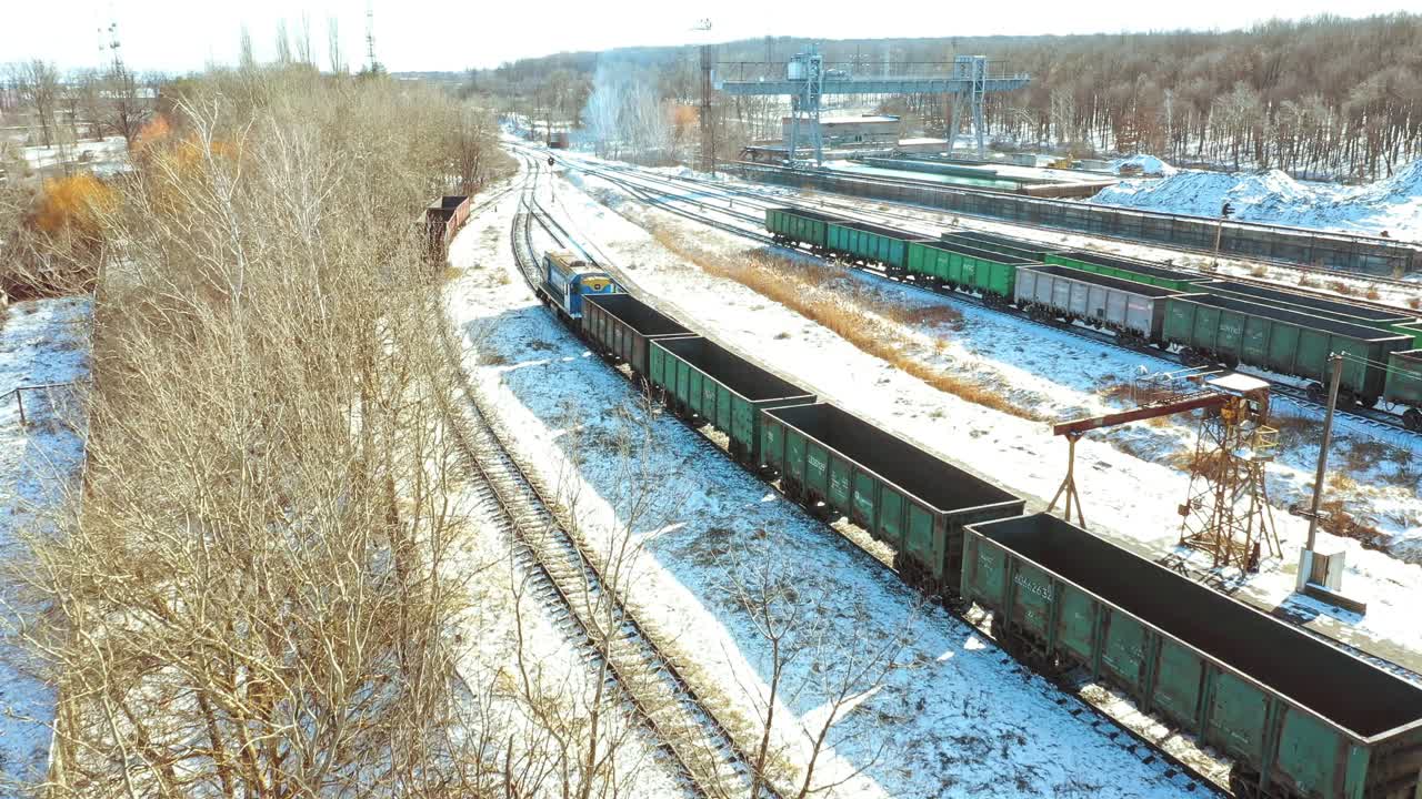 A freight train with containers moves along the rails in the direction of the city in a winter day. Shipping of goods. Aerial view.