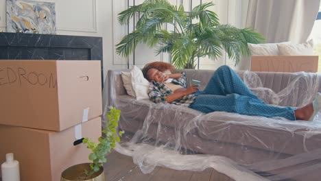 young happy african american woman rejoicing moving to apartment lying on sofa