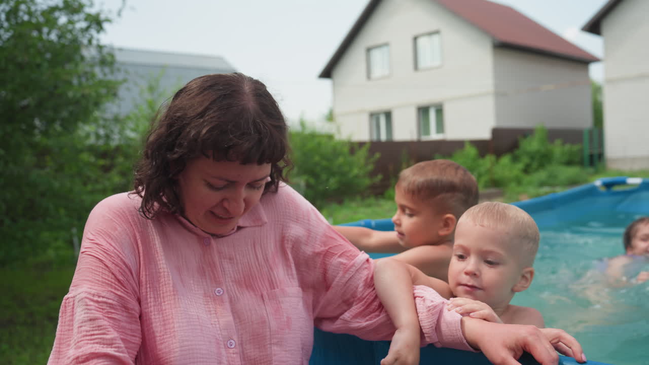 Woman Watches Children Play Happily, Woman Observes Kids Having Fun During Sunny Outdoor Activity, Cheerful Woman Witnesses Children Reveling In Summer Splashes Near Suburban Residence