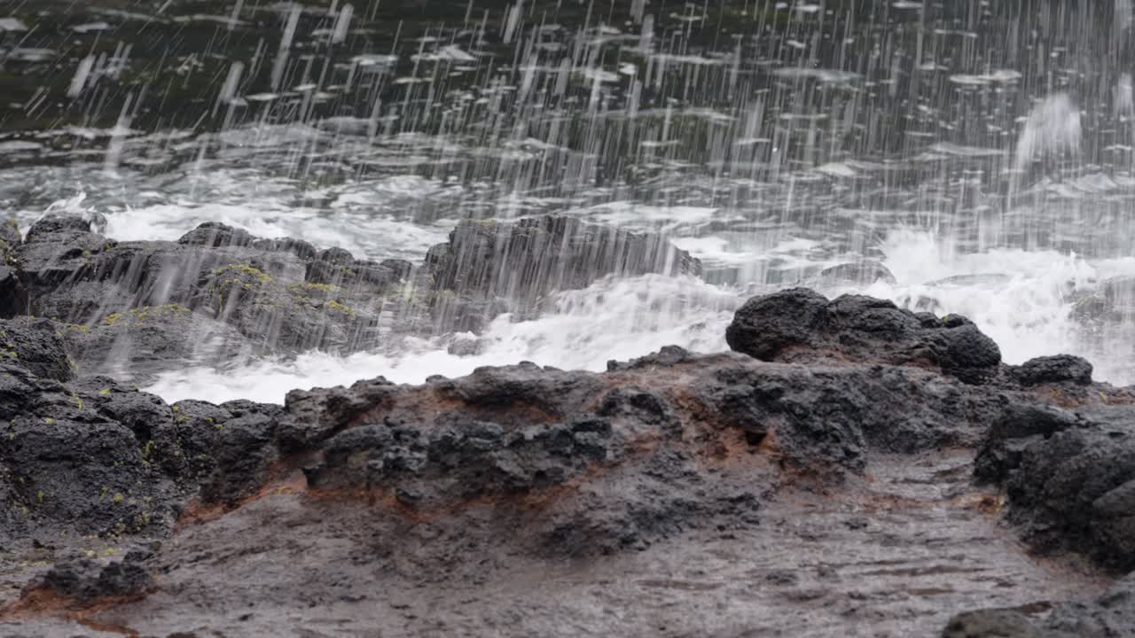 Close-up shot of waves crashing and splashing over rocks, capturing the raw energy and movement of the ocean.