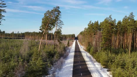 straight forest road with snowy landscape around, aerial dolly backward view