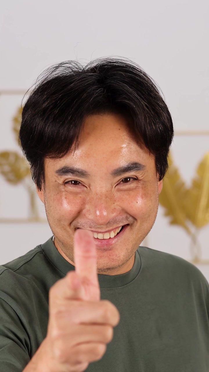Uomo asiatico di mezza età con una camicia verde casual sorride e indica con il pollice in su in un ambiente interno ben illuminato, la telecamera rimane stabile.