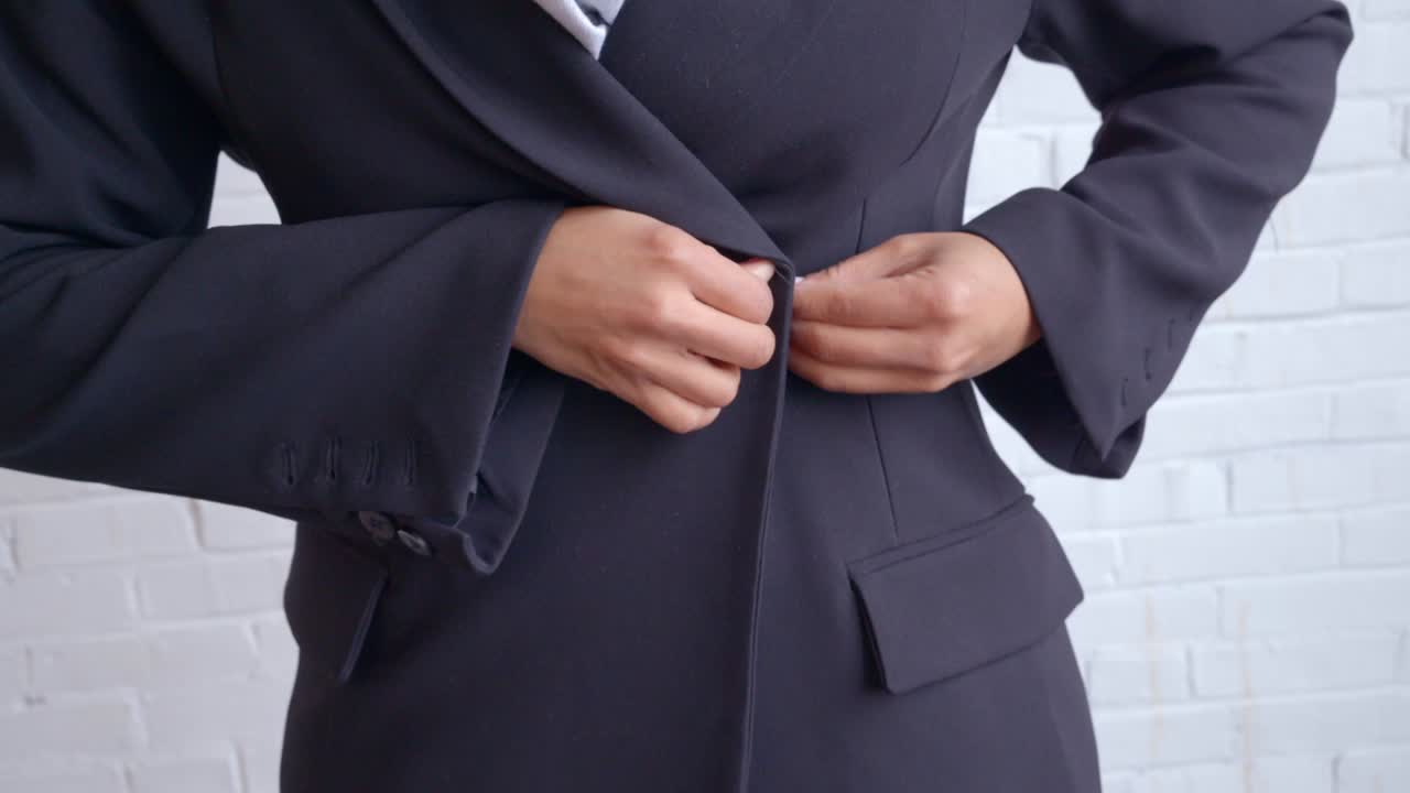 A woman in a black trench coat and white scarf buttoning her coat, set against a clean white background.