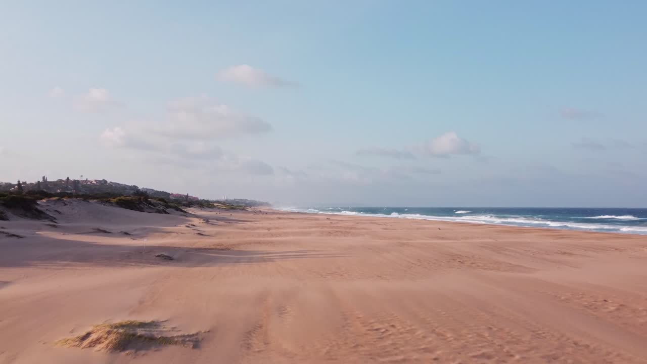 Golden sandy Illovo beach in South Africa with city of Durban on the horizon and waves in Indian Ocean, dolly rising shot