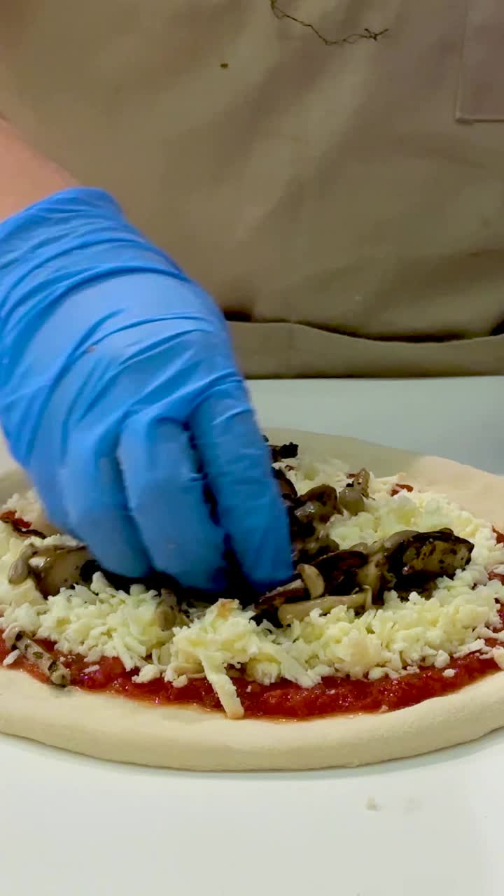 요리사는 치즈와 버섯으로 피자를 준비합니다.