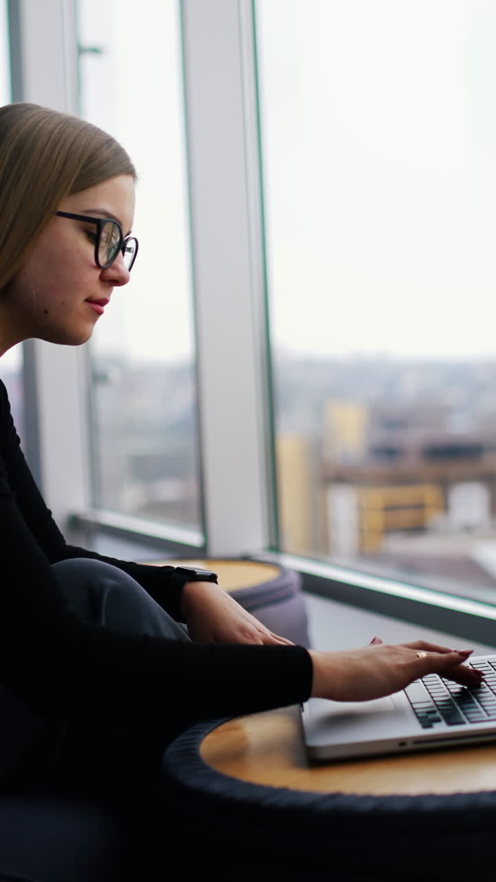 Young beautiful woman with glasses working on laptop. Vertical video