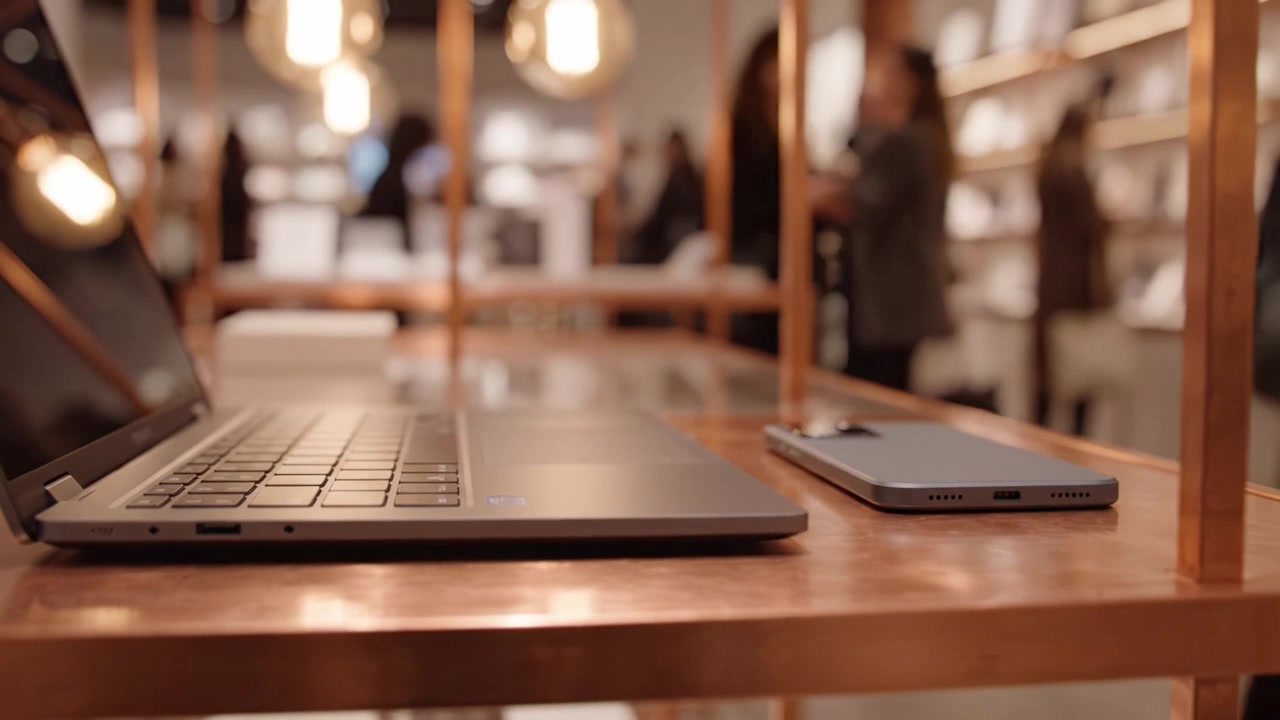 A Modern Workspace Featuring a Sleek Laptop and Smartphone on a Stylish Table in a Chic, Blurred Retail Environment with Elegant Lighting and Accessories