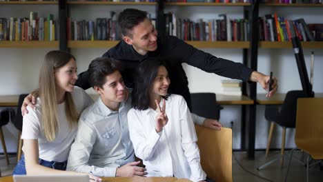 estudiantes europeos, grupo de cuatro toman una selfie en la biblioteca de la universidad o universidad. grupo de cuatro de pie en las estanterías delanteras