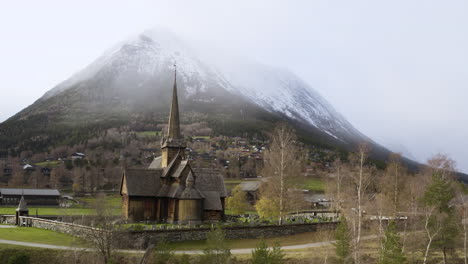 vista escénica de la iglesia de lom stave contra una enorme montaña nevada en invierno en noruega