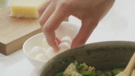 crop woman adding mozzarella balls to pasta