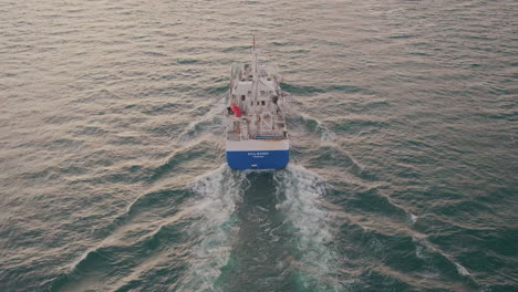 trawler vessel cruising and leaving wake on the sea at dusk in tromso, norway