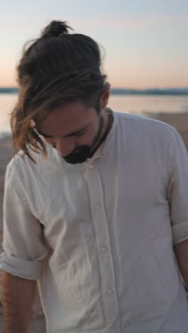 a man walking with a guitar by a lake at sunset