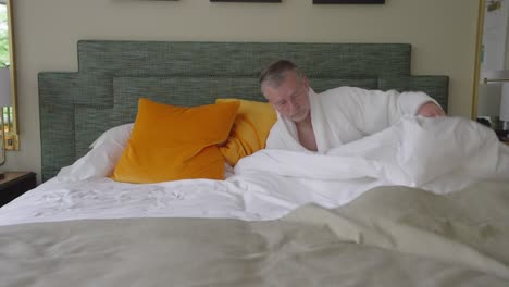 hombre vestido con bata blanca metiéndose en la cama y tratando de sentirse cómodo