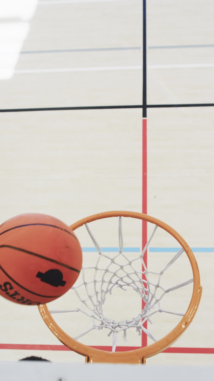 Vertical video of male african american basketball player training in indoor court, in slow motion