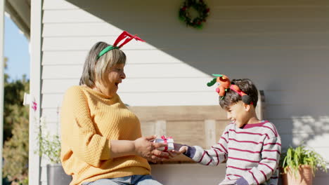 Feliz-Abuela-Birracial-Y-Nieto-Sentados-En-La-Terraza-Dando-Regalos-De-Navidad,-Cámara-Lenta